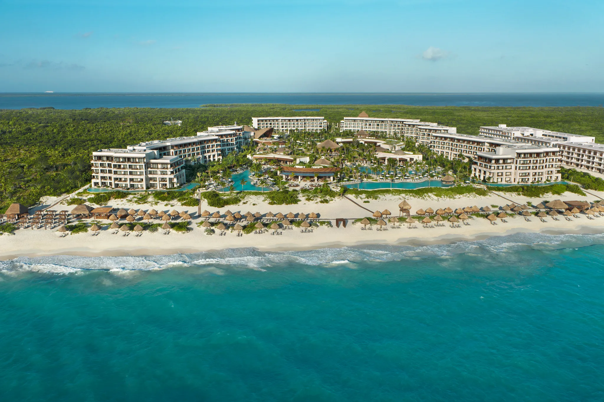 Oceanfront aerial of Secrets Playa Blanca Costa Mujeres showcasing resort buildings, pools, and beachfront lined with palapas.