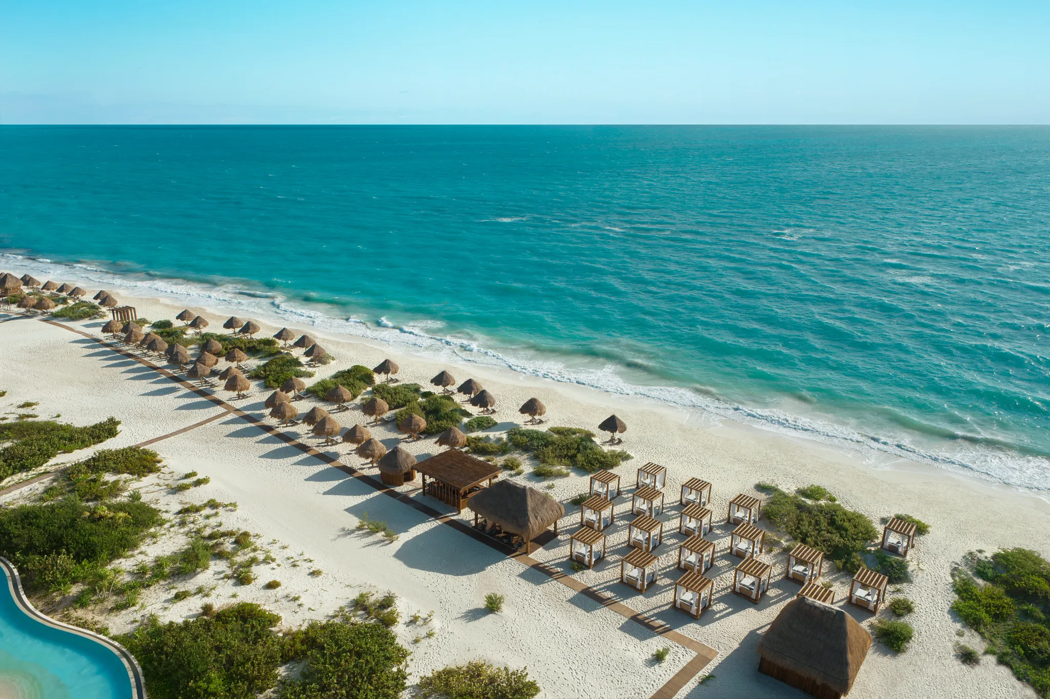 Beach cabanas and palapas set up on white sand at Secrets Playa Blanca Costa Mujeres with turquoise ocean views.
