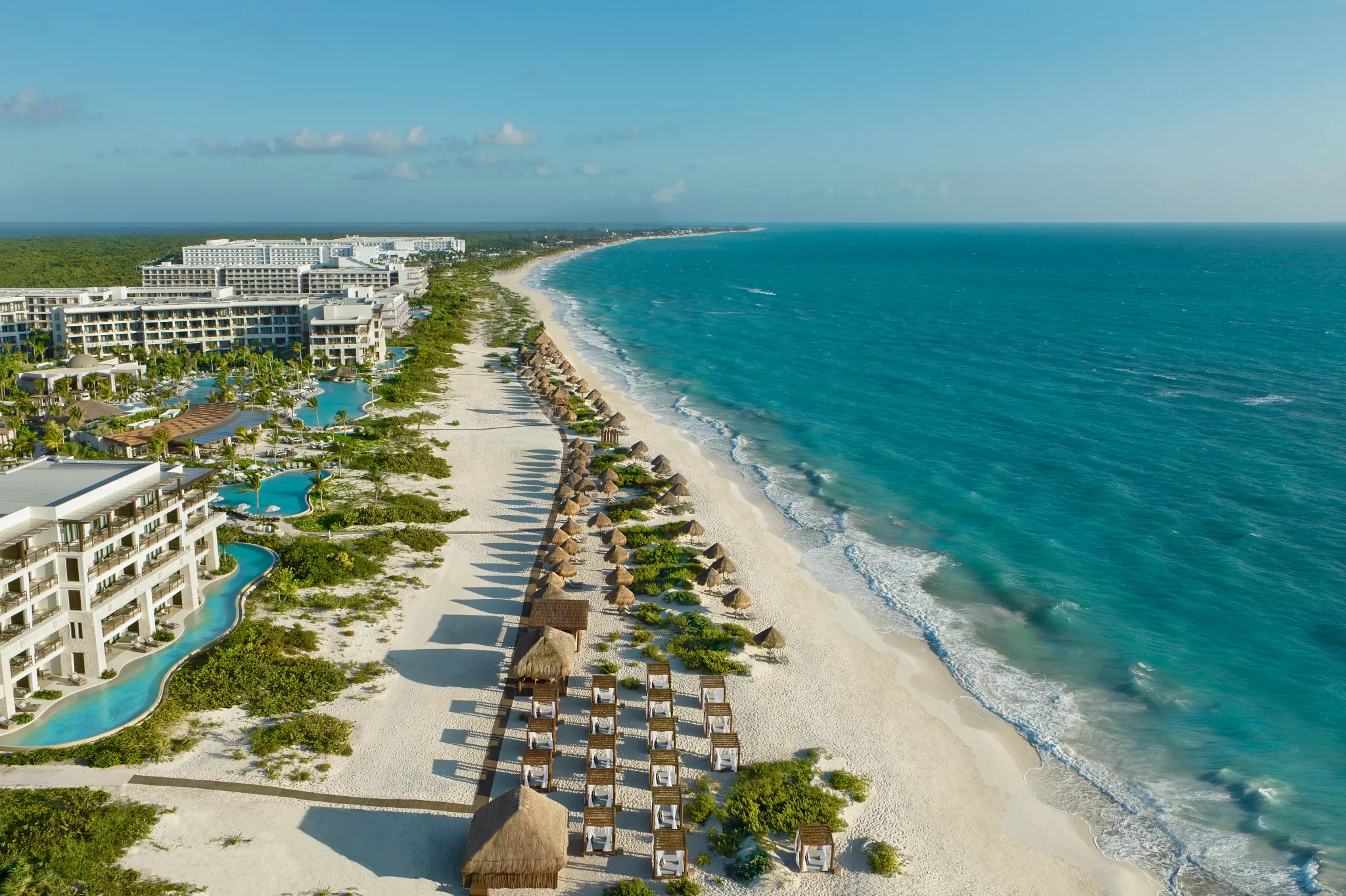 Stunning aerial of Costa Mujeres beach with turquoise water and rows of palapas at Secrets Playa Blanca resort.