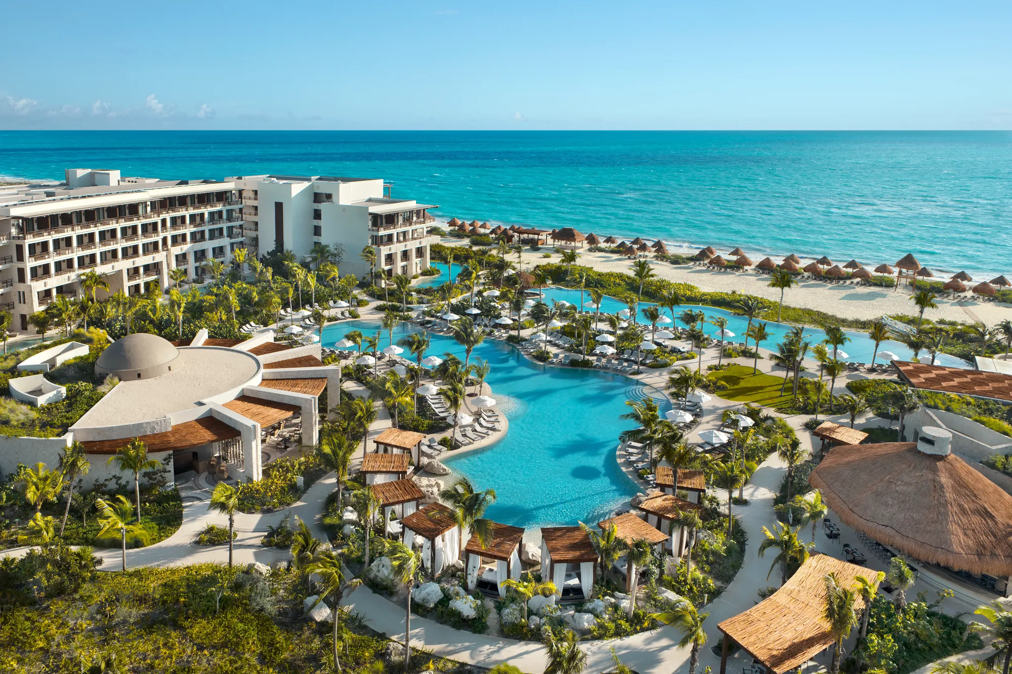 Multiple infinity pools surrounded by palm trees overlooking the Caribbean Sea at Secrets Playa Blanca Costa Mujeres.